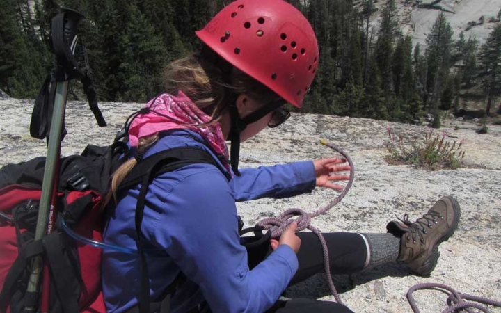 a person wearing a helmet works to tie a knot in their harness